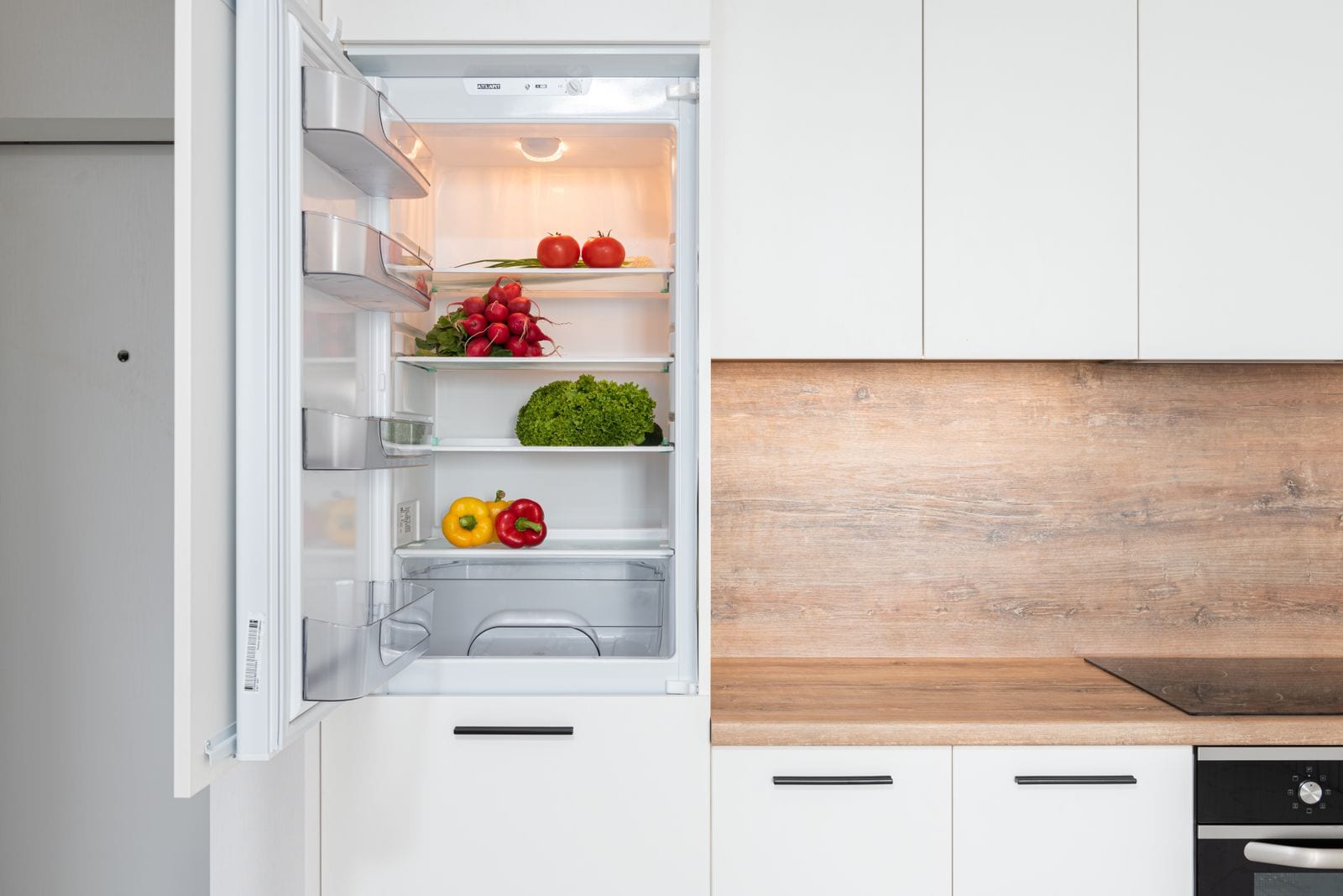 Open fridge filled with fresh tomatoes, lettuce and peppers