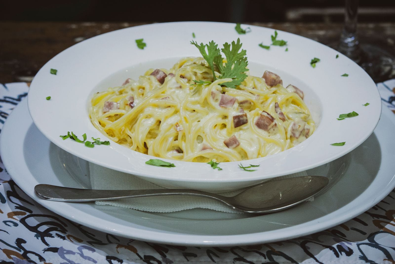 Creamy pasta with ham and herbs in a white bowl