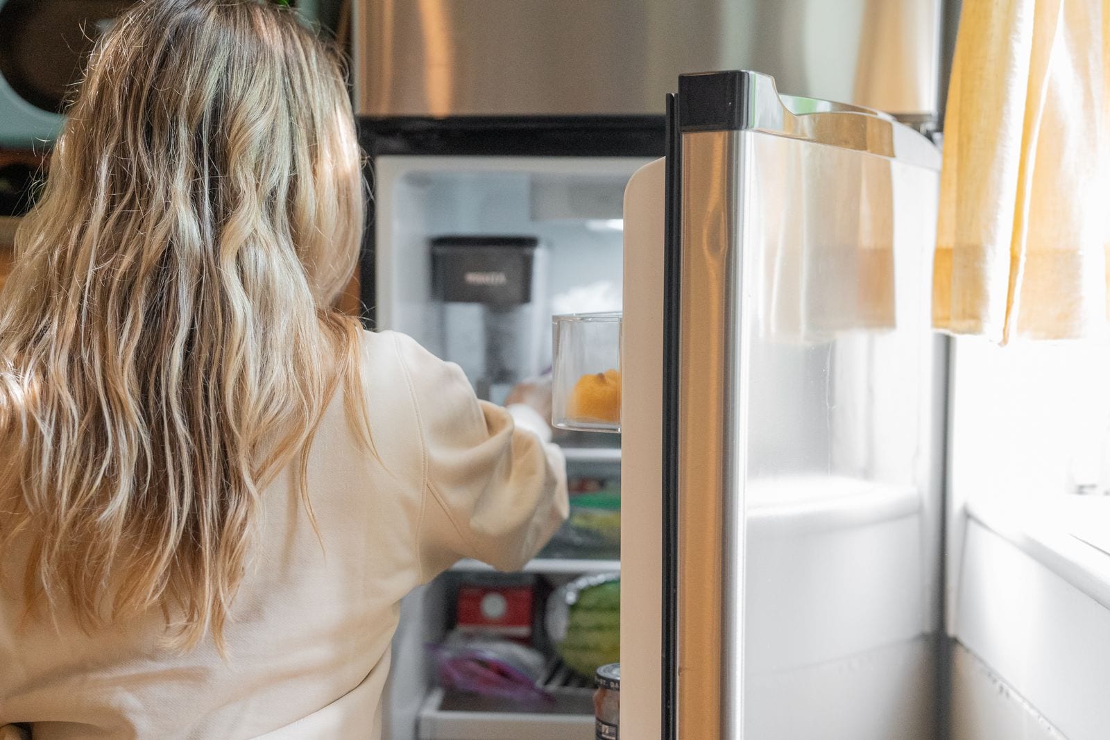 Person seen from behind taking food out of a refrigerator in a bright kitchen