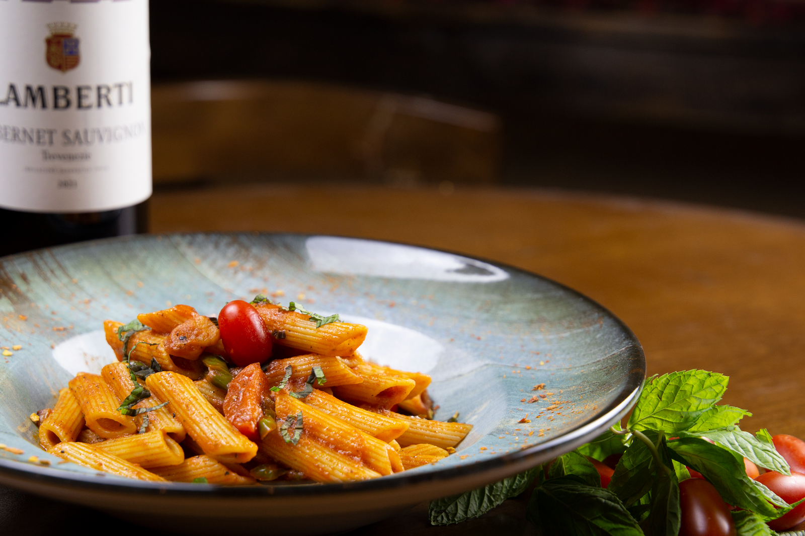 Plate of penne pasta with tomato sauce and basil, served with a glass of wine