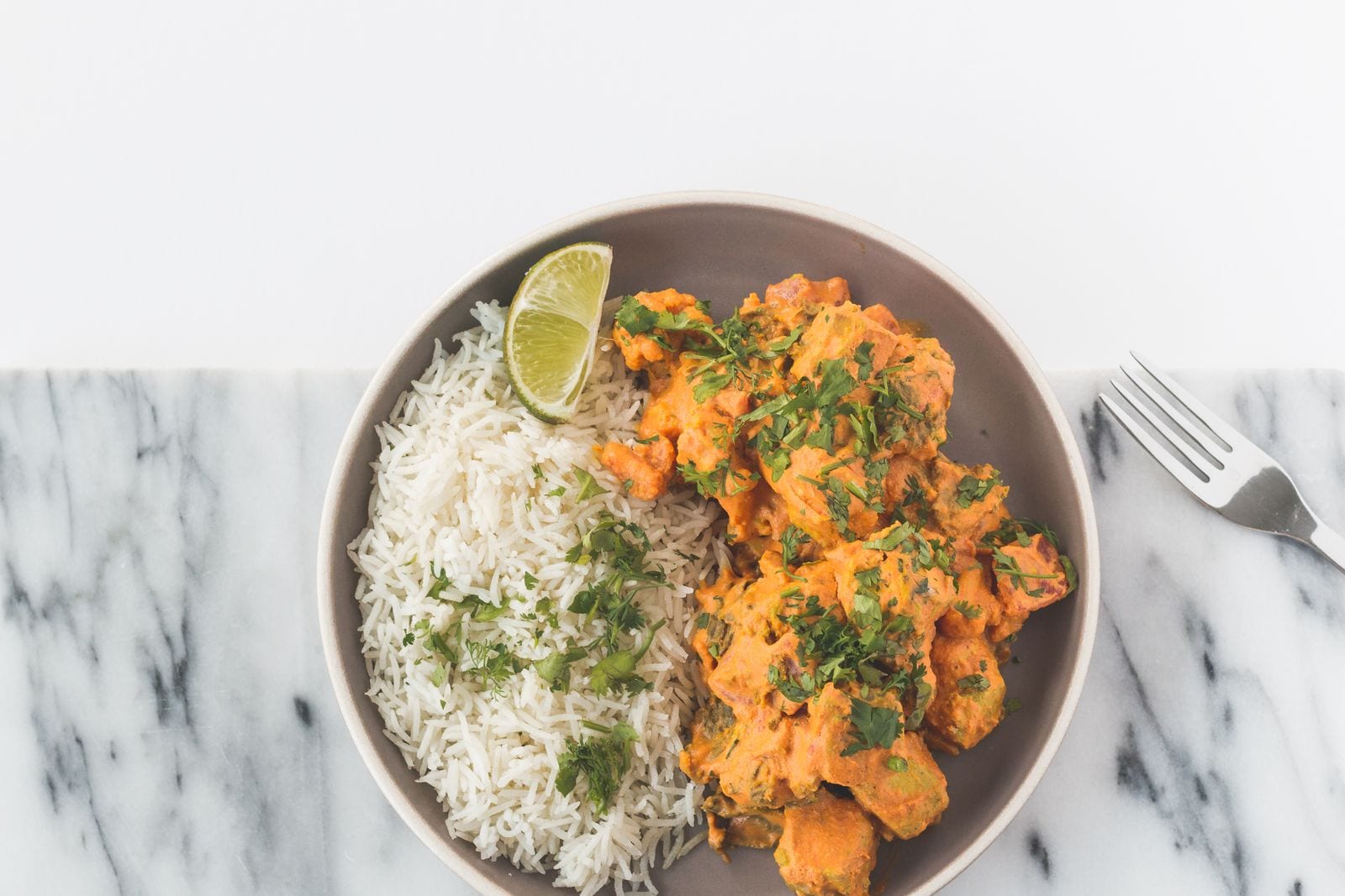 A bowl of curry served over basmati rice, garnished with herbs and lime
