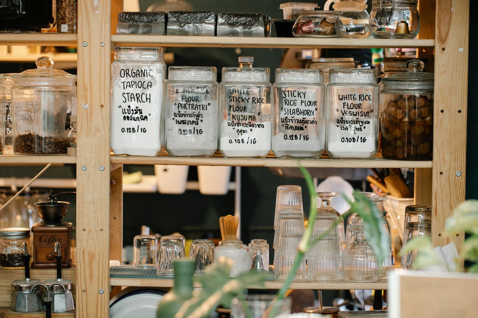 Glass jars of dry food and glassware on a wooden shelf